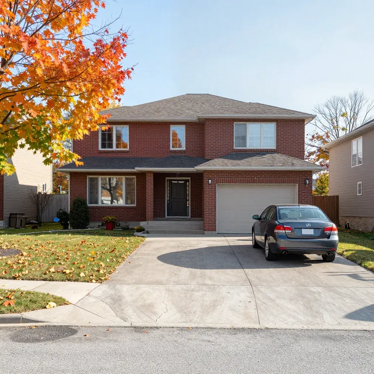 A red-brick two-storey house with a car in the driveway and autumn maple leaves on the lawn.
